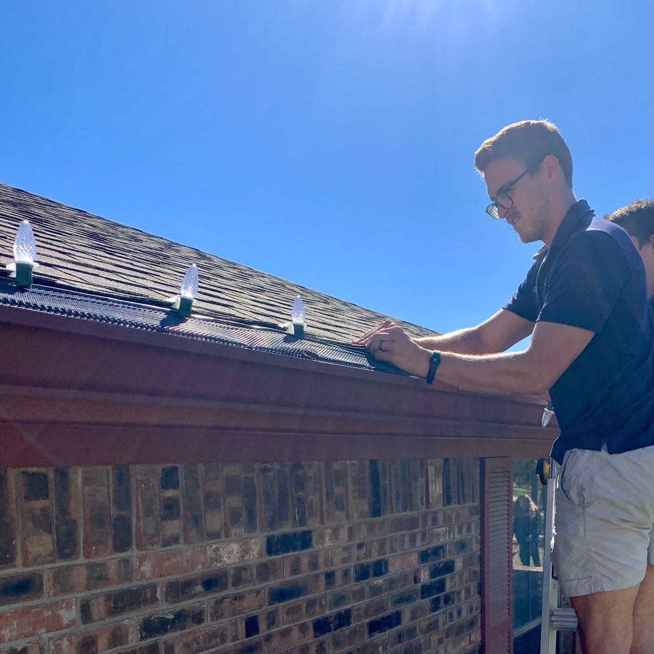 RiverHills crew member on a ladder installing Christmas lights along a roofline