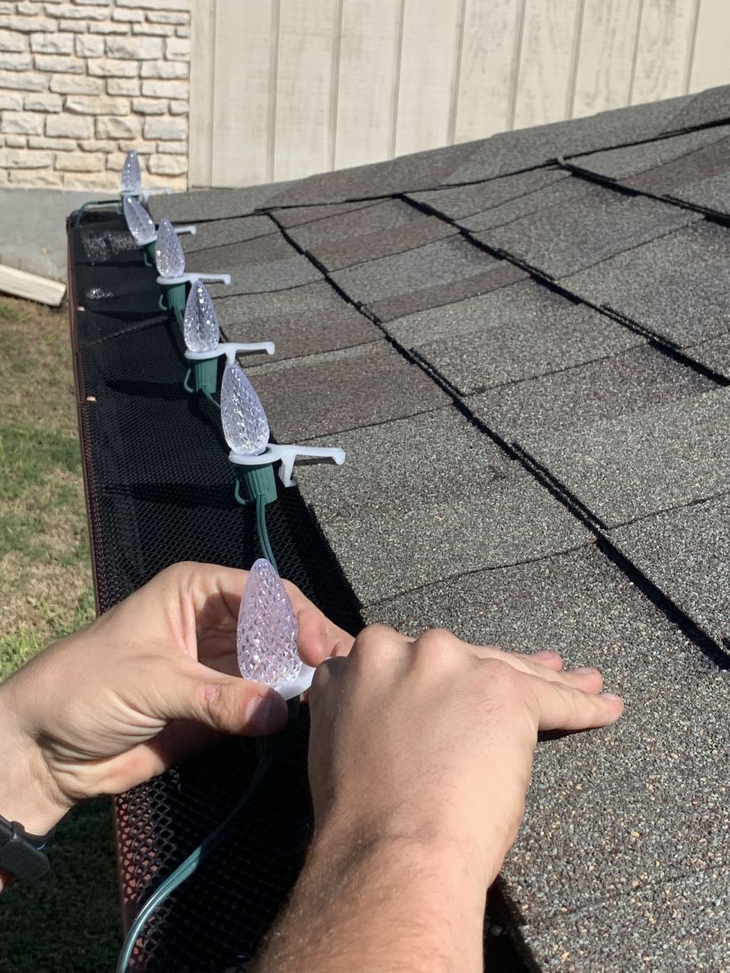 Hand clipping a C9 Christmas light bulb onto a gutter with a professional light clip